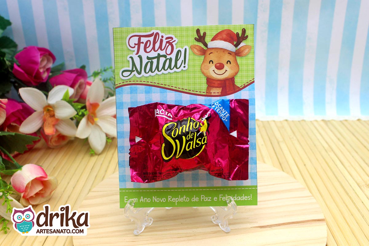 Cartão porta-bombom de rena com bombom Sonho de Valsa encaixado, em fundo verde xadrez azul e mensagem de Feliz Natal.