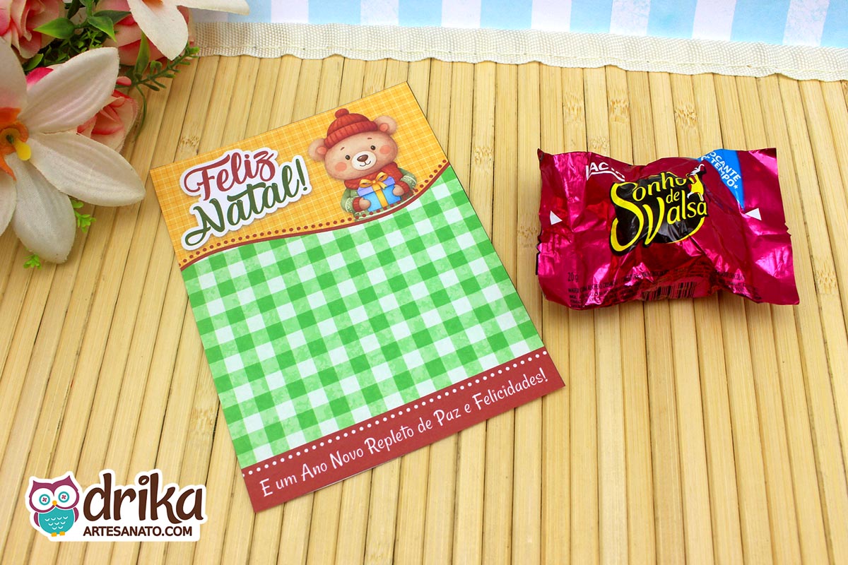 Cartão porta-bombom de Natal com urso de gorro vermelho, fundo xadrez verde e bombom Sonho de Valsa ao lado.