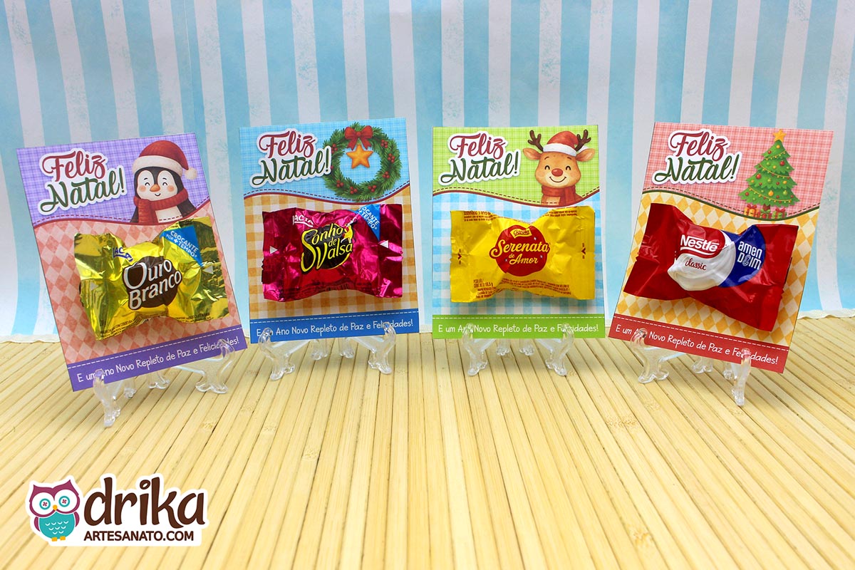 Quatro cartões porta-bombom de Natal com personagens e bombons diferentes em miniaturas de acrílico sobre mesa de madeira