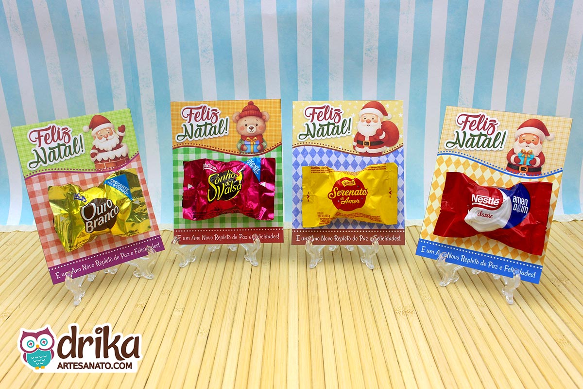 Quatro cartões porta-bombom de Natal com Papai Noel e bombons sortidos em miniaturas de acrílico sobre mesa de madeira