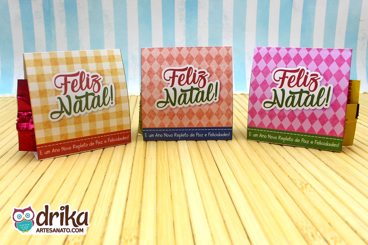 Três porta-bombons quadrados com estampas xadrez amarela, geométrica rosa e quadriculada rosa, com mensagem de Feliz Natal