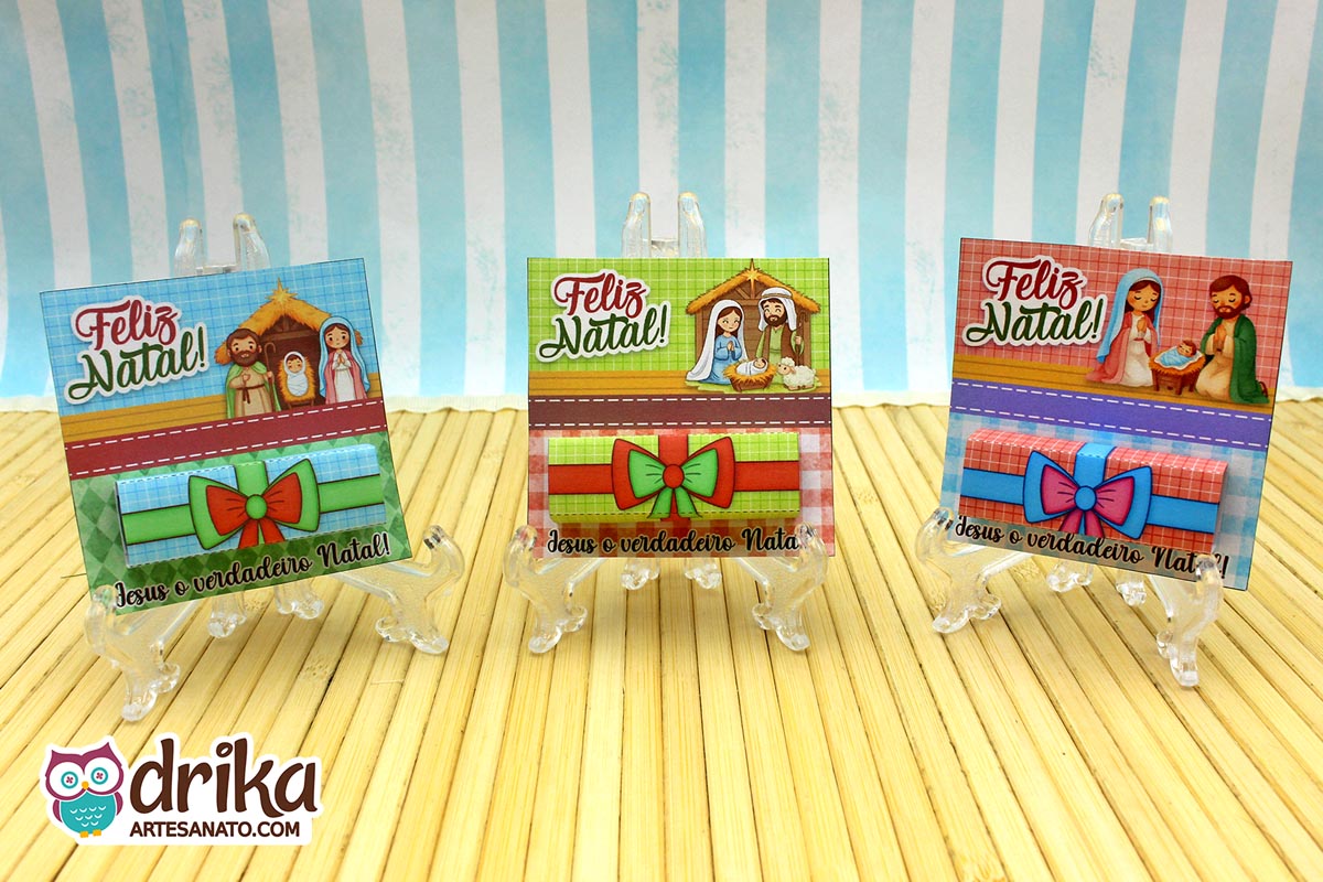 Três porta-bis de Natal com a Sagrada Família em suportes transparentes sobre esteira de bambu