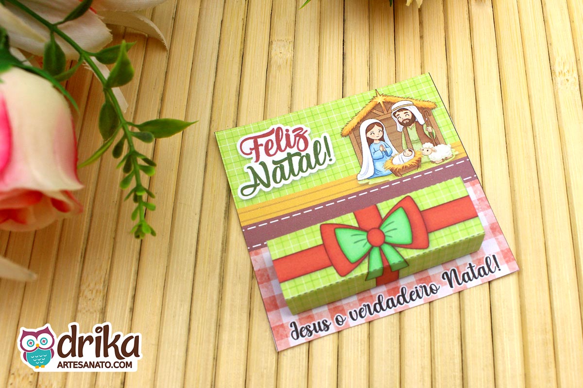 Porta-bis de Natal montado com a Sagrada Família e embalagem do Bis em mesa de bambu e fundo floral.