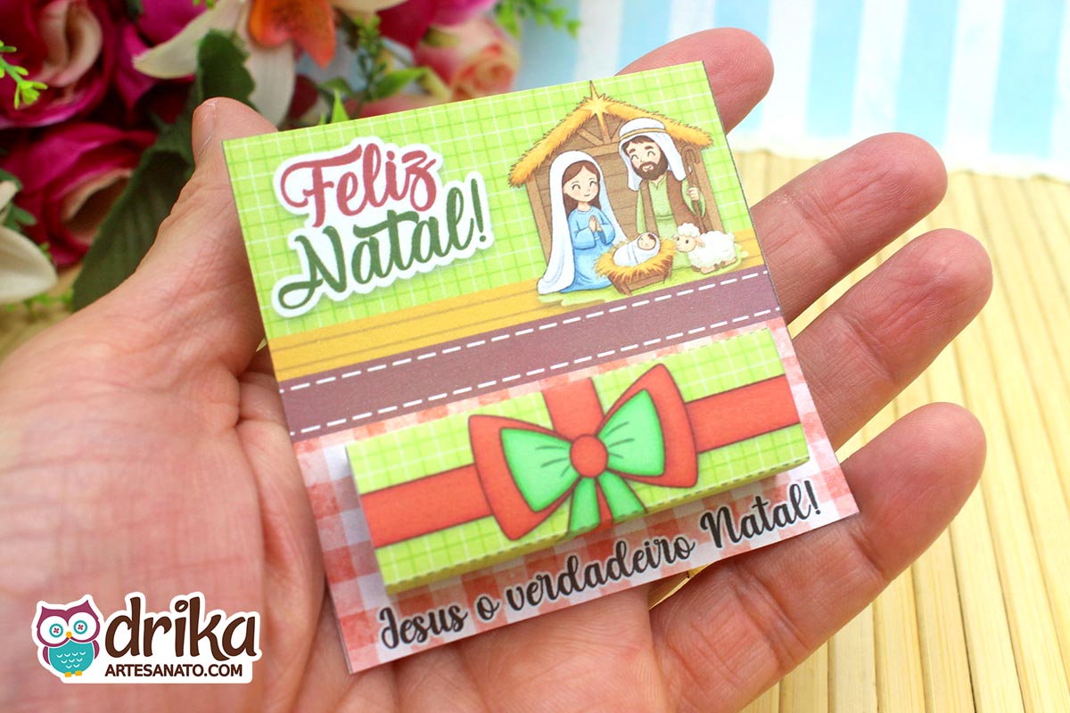 Porta-bis de Natal com a Sagrada Família e Bis embalado na mão de uma pessoa, com fundo floral.