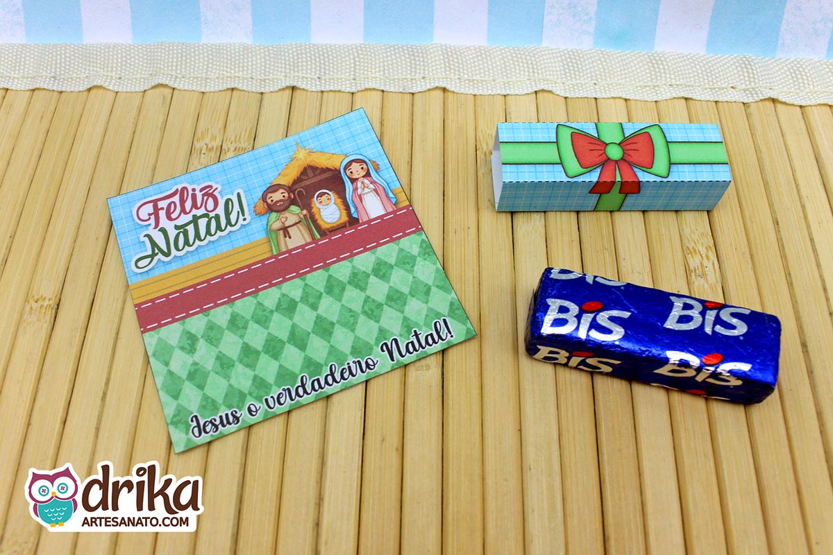 Cartão porta-bis de Natal com ilustração da Sagrada Família, rótulo e chocolate Bis em mesa de bambu.