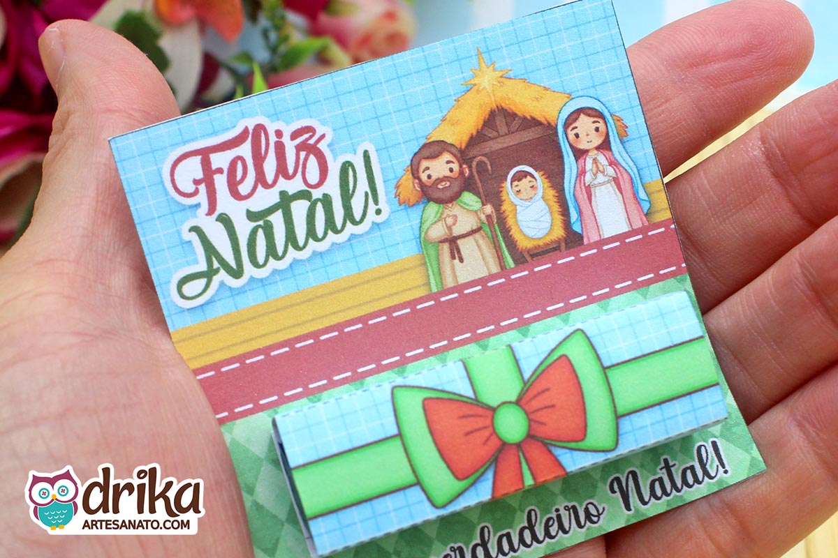 Close-up de mão segurando cartão porta-bis de Natal com ilustração da Sagrada Família.