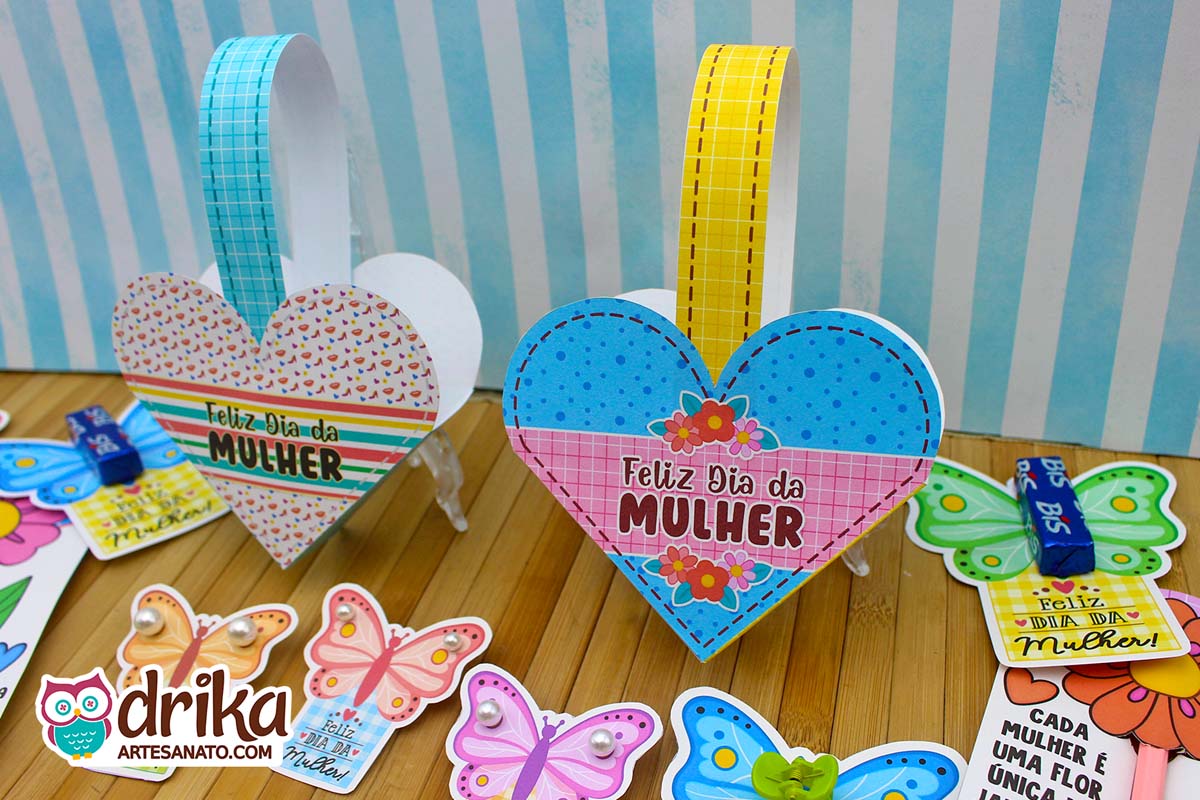 Duas cestinhas de papel em formato de coração, uma com estampa de sapatinhos e listras, outra azul de bolinhas e flores, com outros mimos