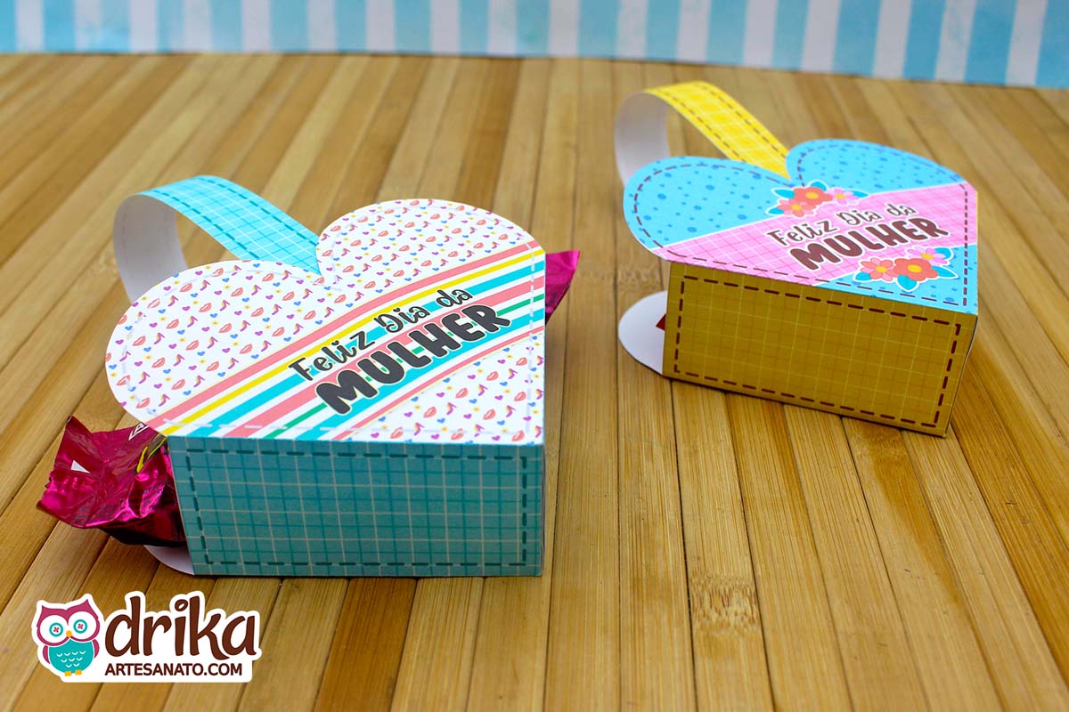 Duas cestinhas de papel em formato de coração, uma com estampa de sapatinhos e listras, outra azul de bolinhas e flores, com docinho