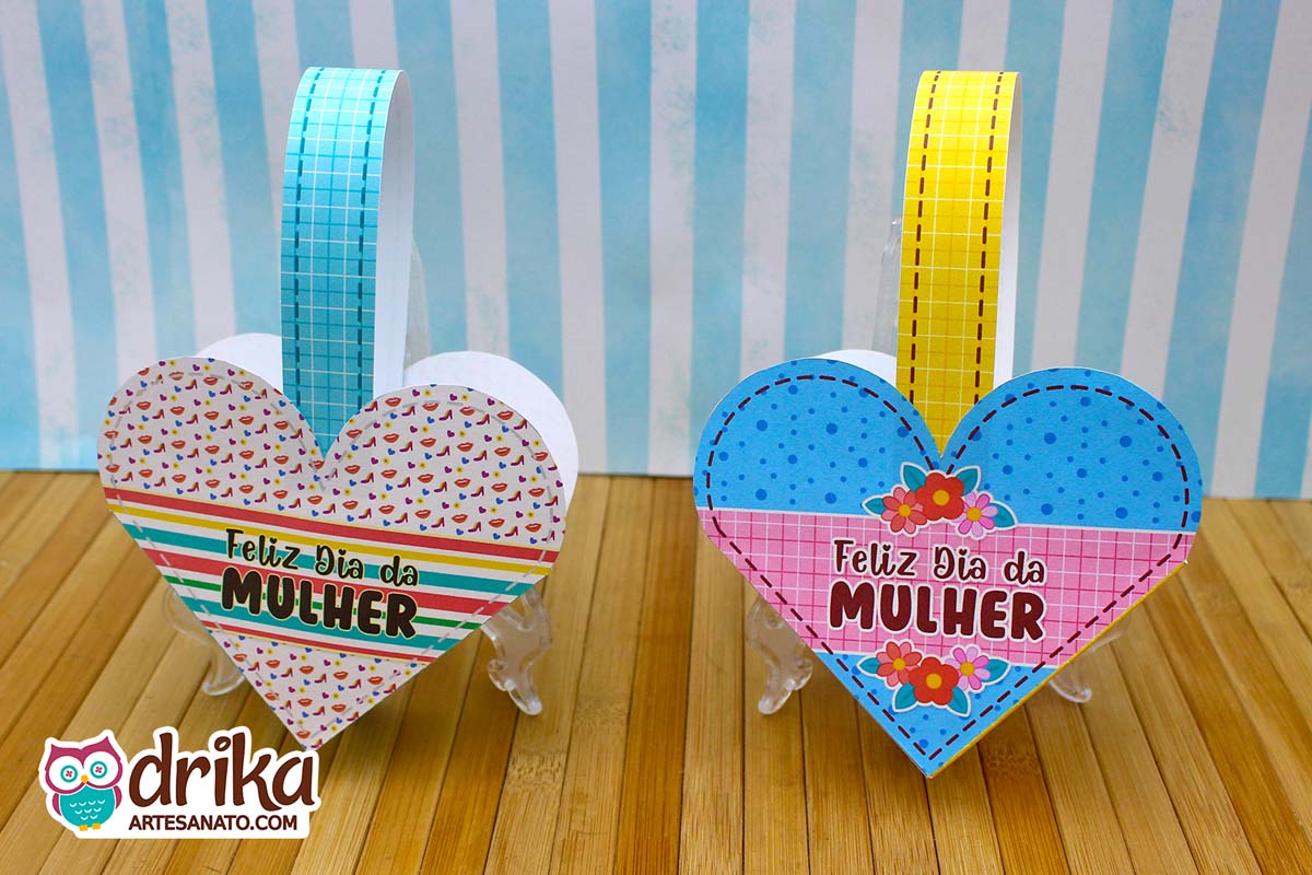 Duas cestinhas de papel em formato de coração, uma com estampa de sapatinhos e listras, outra azul de bolinhas e flores