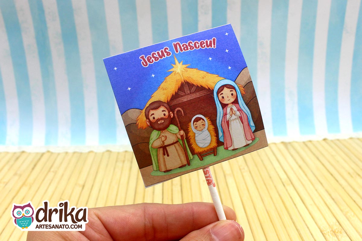 Capinha para pirulito com ilustração da Sagrada Família em estábulo sob céu estrelado e frase "Jesus Nasceu"