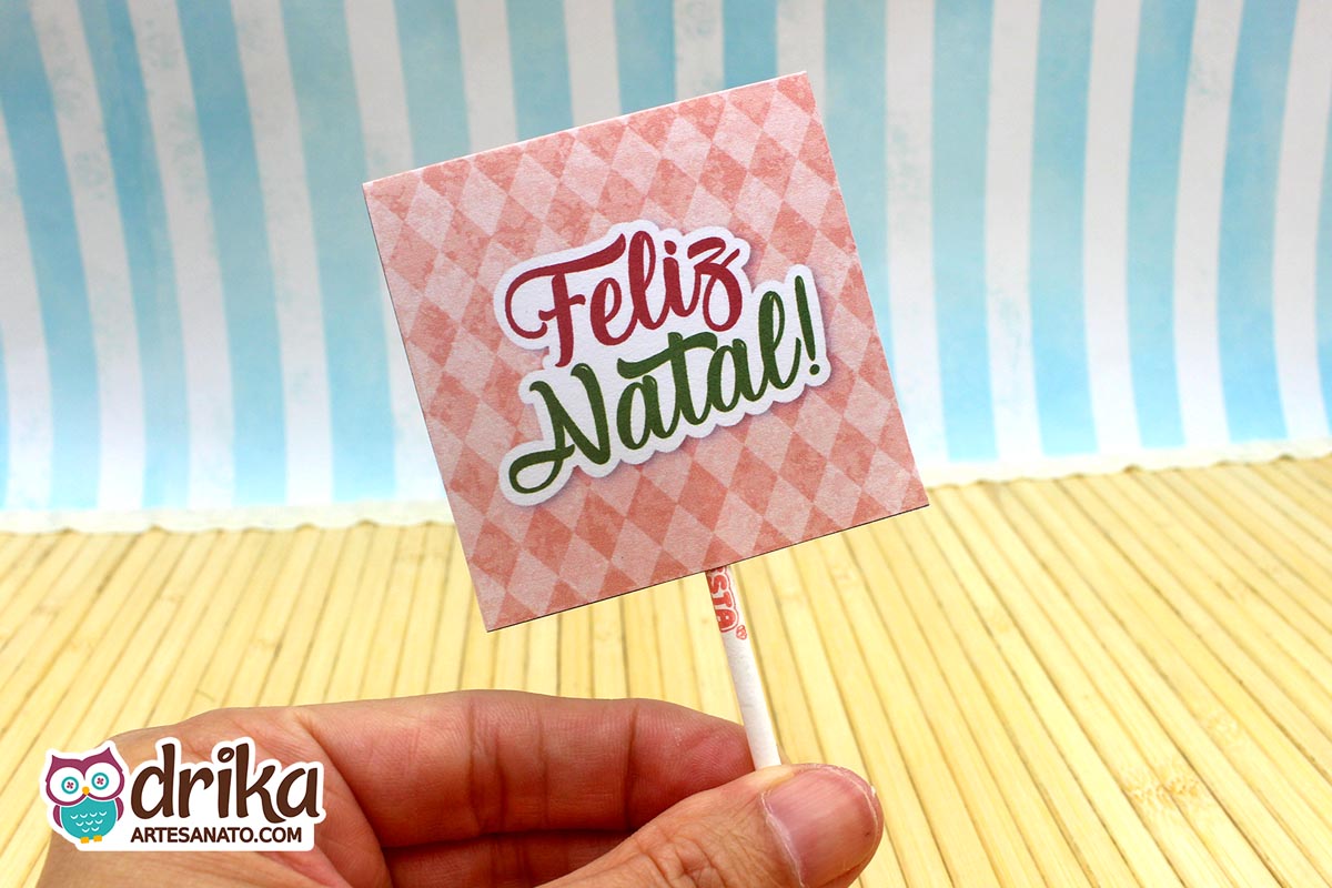 Verso da capinha de pirulito com fundo rosa quadriculado e a frase "Feliz Natal!" em verde.
