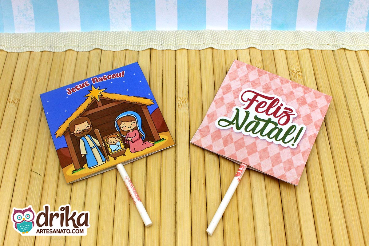 Duas capinhas de pirulito natalinas, frente e verso, em fundo de madeira e listras azuis.