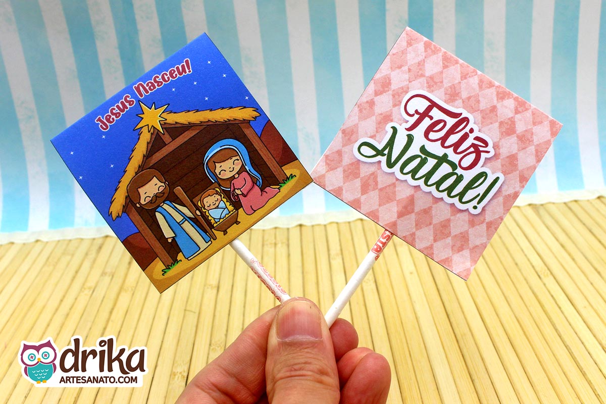 Capinhas de pirulito lado a lado: frente com presépio e verso com "Feliz Natal!" em fundo rosa.