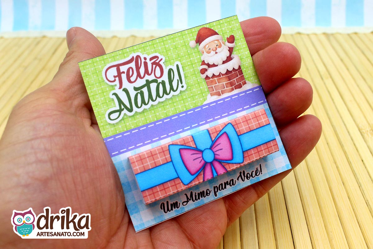 Mão segurando o cartão porta-bis de Papai Noel na chaminé com chocolate Bis já encapado e inserido