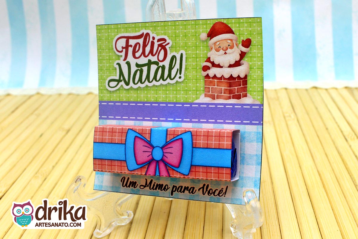 Cartão porta-bis de Papai Noel na chaminé com chocolate Bis encapado, em suporte transparente sobre superfície de bambu