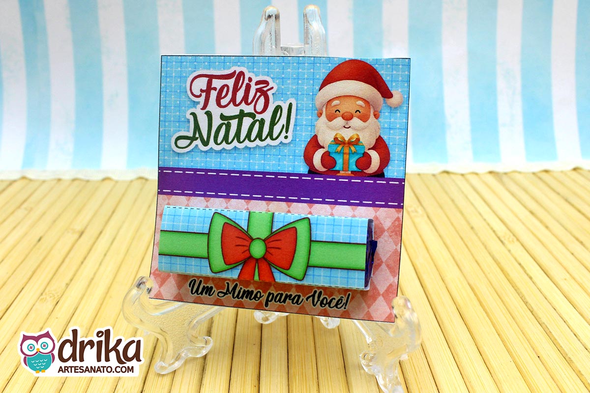 Cartão porta-bis de Papai Noel montado com chocolate Bis embrulhado em cinta de presente verde, exibido em suporte transparente