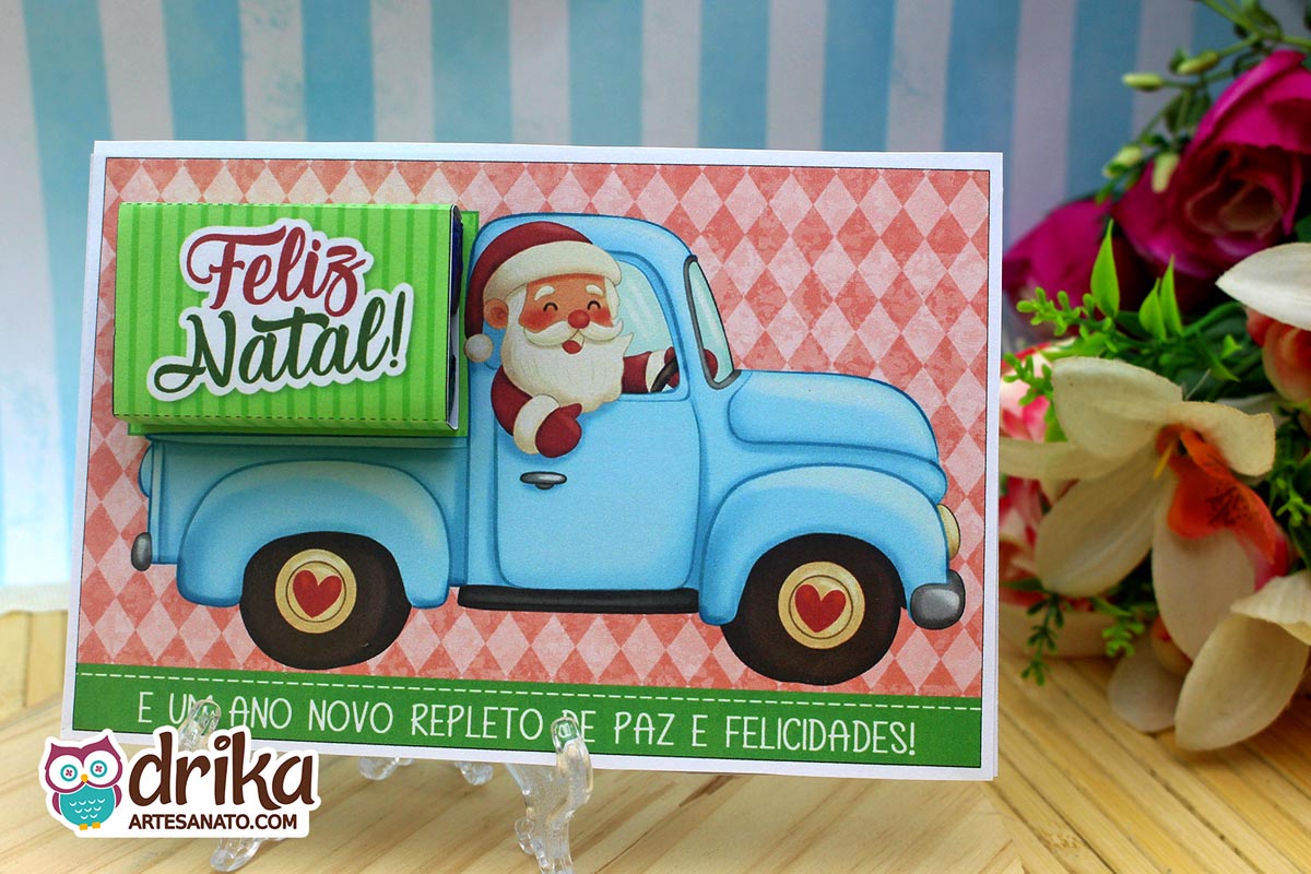 Cartão porta-bis de Papai Noel em caminhonete azul clara, com chocolates Bis verdes e fundo xadrez coral