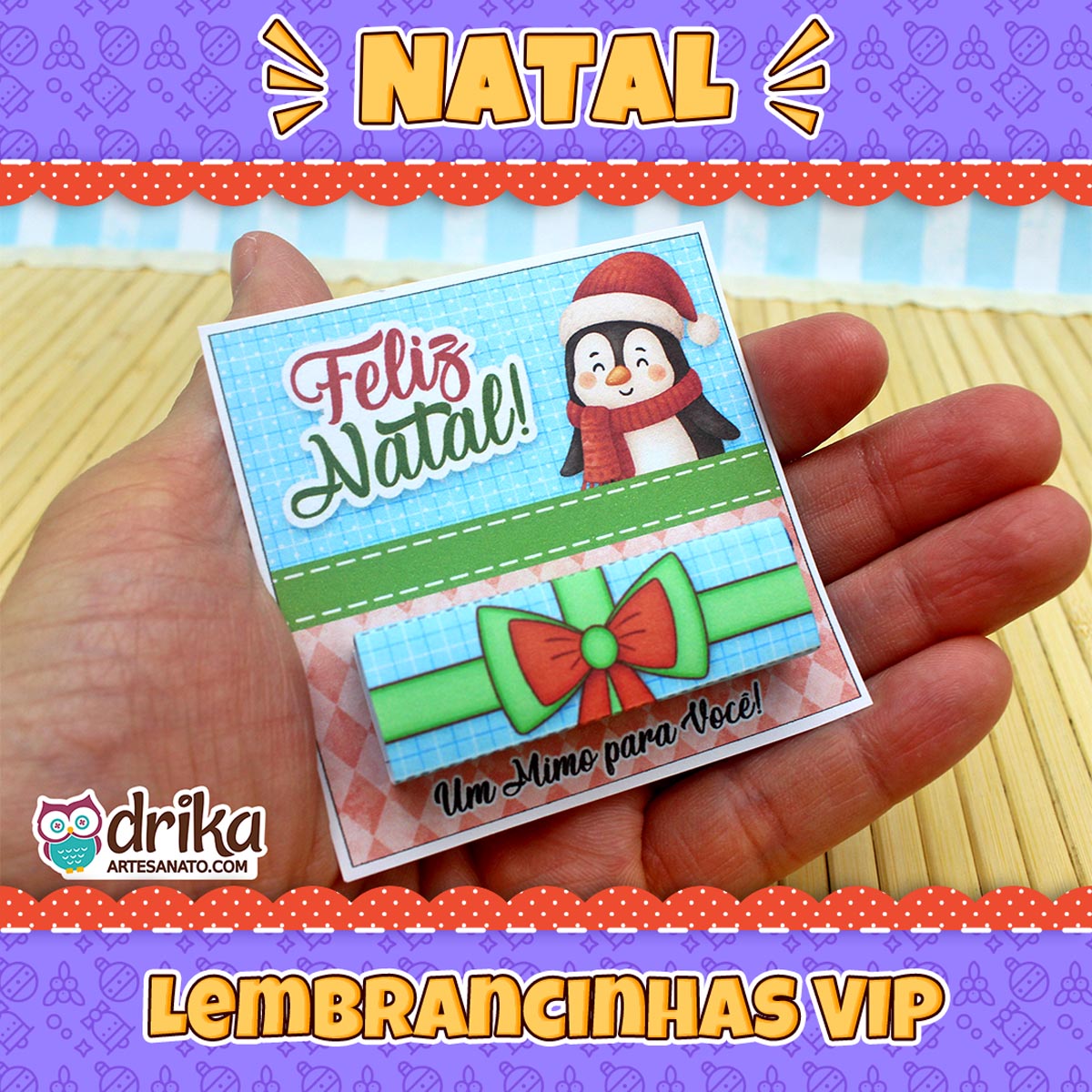 Mão segurando um cartão porta-bis de pinguim natalino com gorro, cachecol e laço vermelho e verde