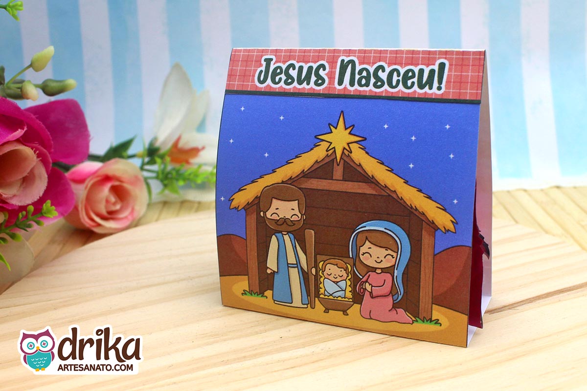 Porta-bombom "Jesus Nasceu" montado, com ilustração da Sagrada Família em manjedoura sob céu estrelado e faixa rosa com a frase.