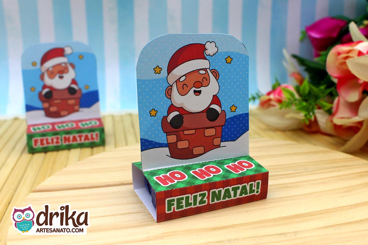 Porta-bis duplo de papel com Papai Noel fofo saindo da chaminé, fundo azul com estrelas. Base verde e vermelha com "HO HO HO FELIZ NATAL"