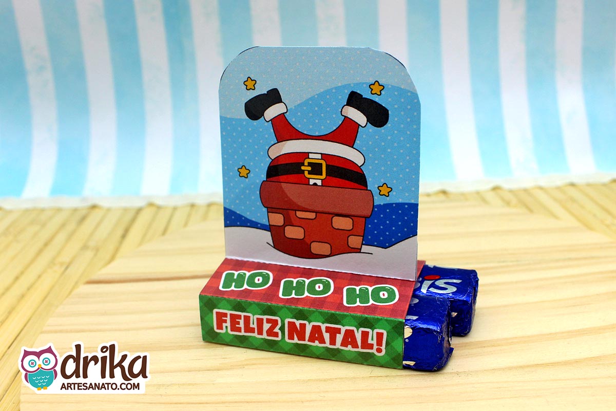 Porta-bis duplo de papel com Papai Noel de pernas para o ar em chaminé de tijolinhos, com dois chocolates Bis azuis