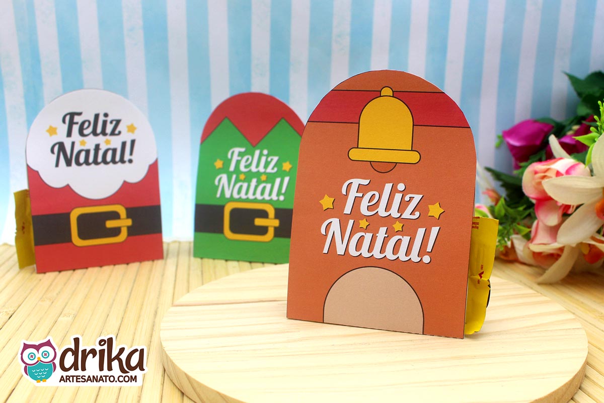 Três porta-bombons de Natal em uma base de madeira: um de rena, um de Papai Noel e um de elfo, todos com "Feliz Natal!"