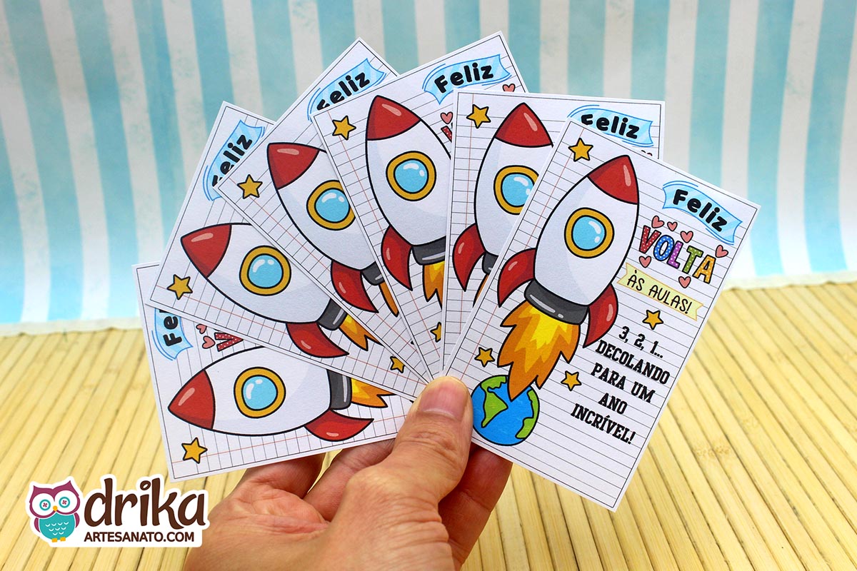 Mão segurando um leque de cartões de Volta às Aulas com foguetes brancos e vermelhos decolando da Terra, em fundo quadriculado