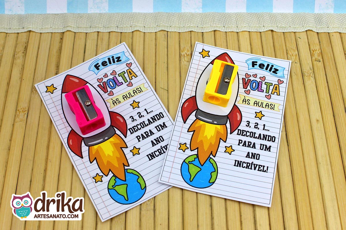 Dois cartões de Volta às Aulas com foguetes, um com apontador rosa e outro com apontador amarelo, sobre esteira de bambu