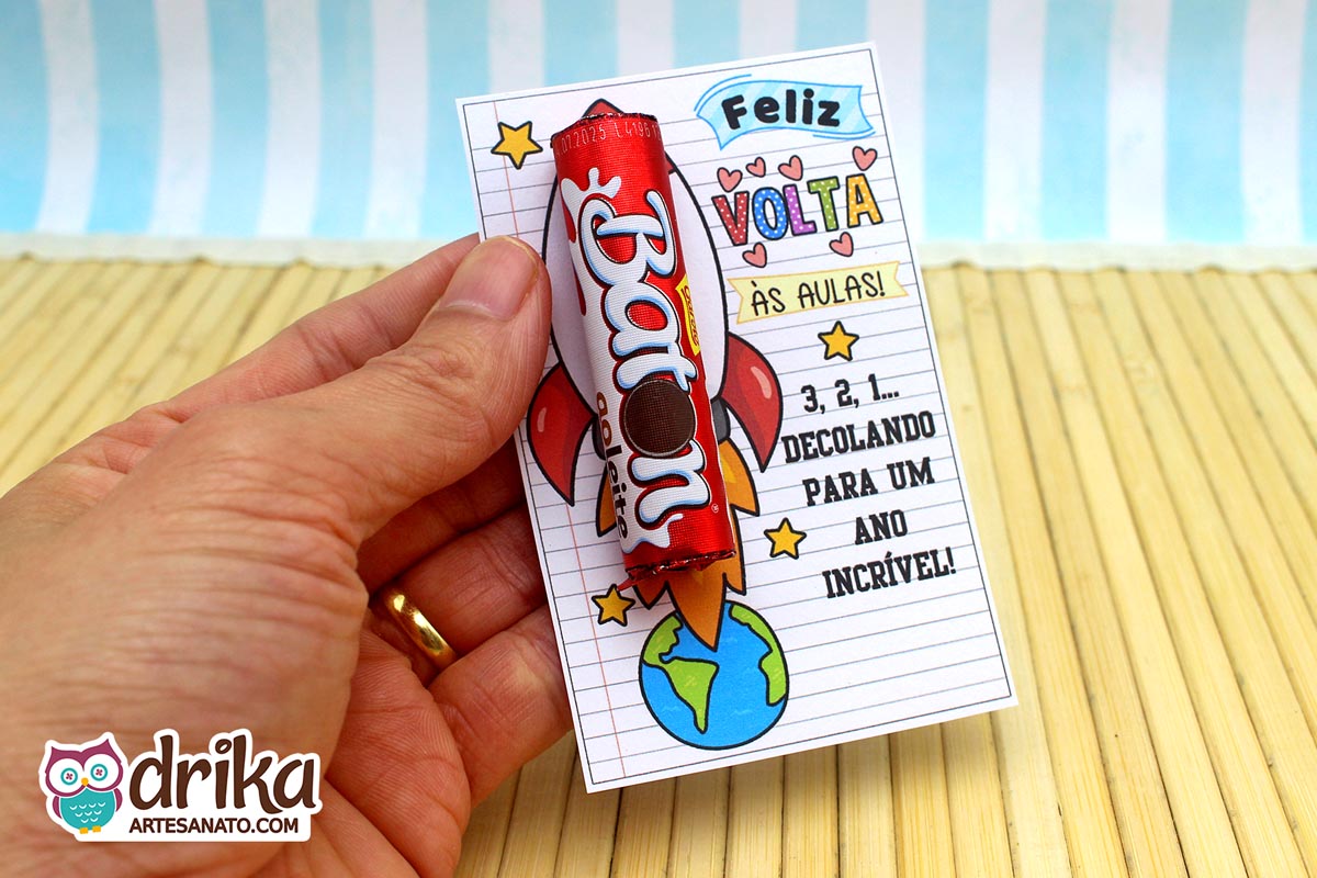 Mão segurando um cartão de foguete com um chocolate Baton vermelho afixado, em close-up