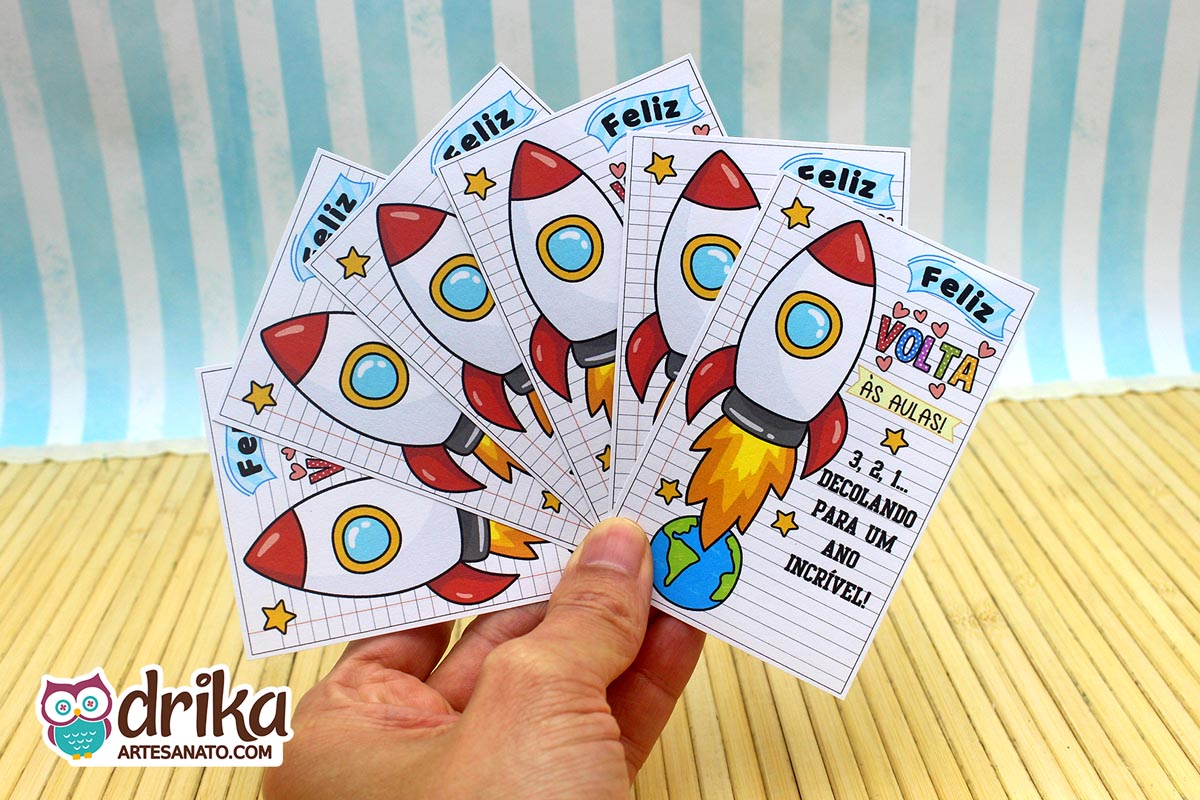 Mão segurando vários cartões porta-bis de Volta às Aulas com foguete vermelho e branco decolando da Terra e frase motivacional