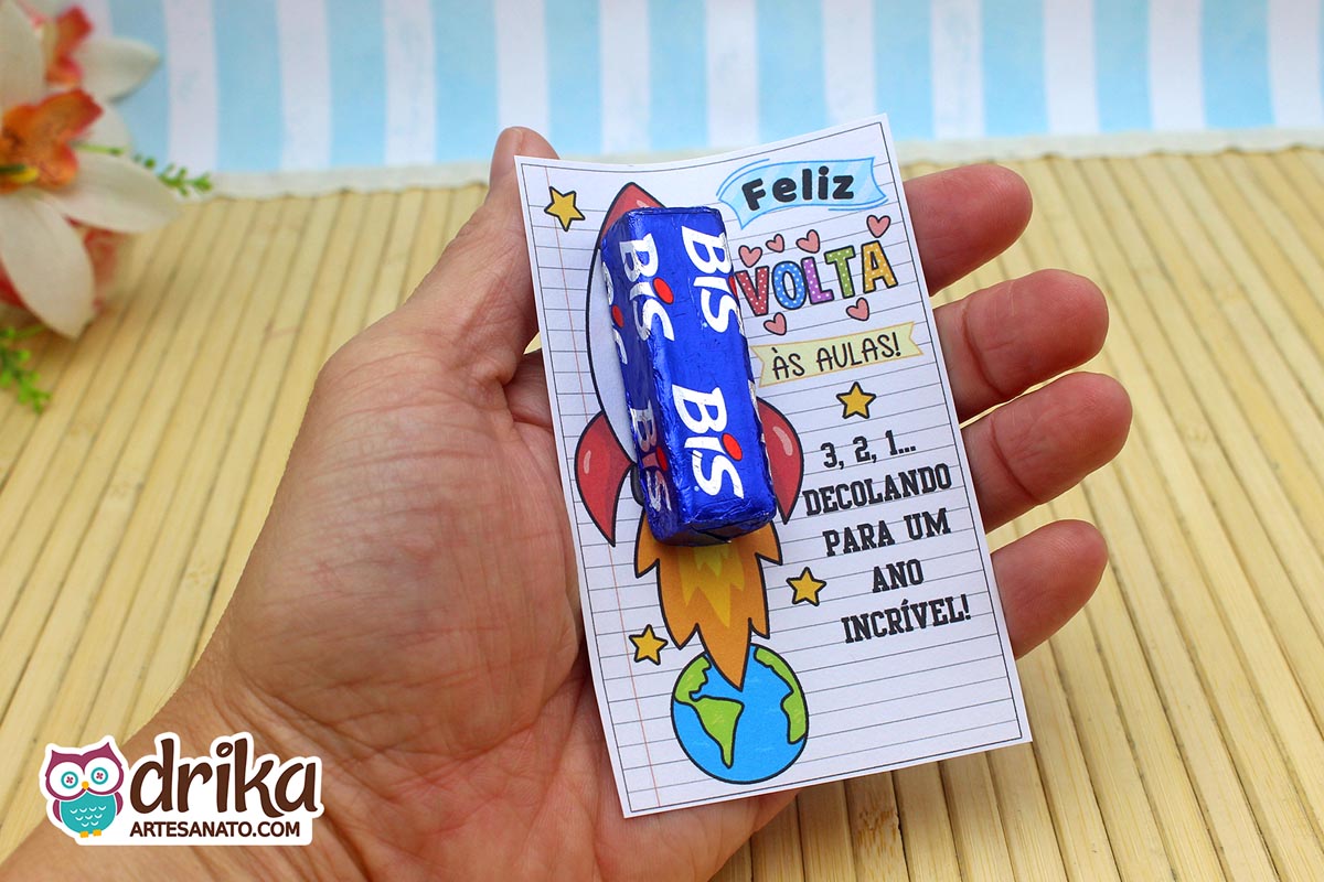 Close-up de mão segurando cartão porta-bis de foguete com chocolate Bis azul encaixado, destacando o design lúdico