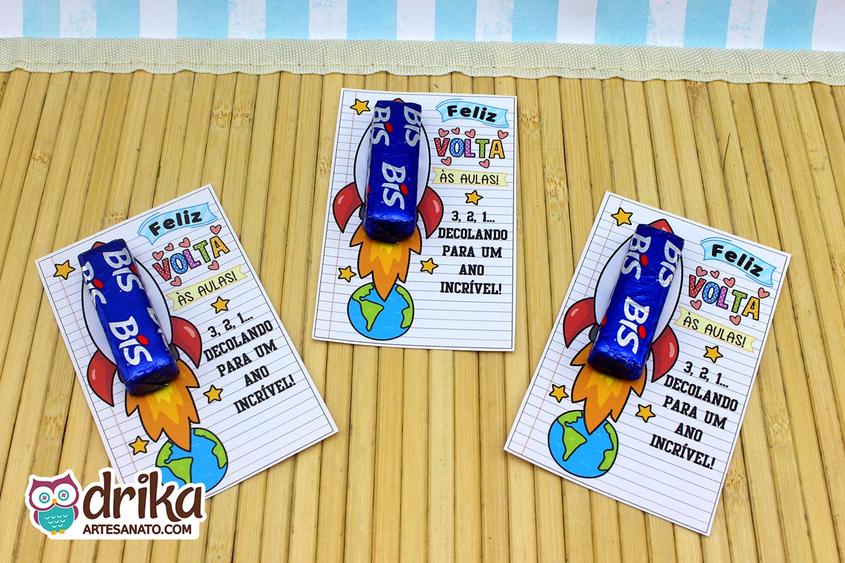 Três cartões porta-bis com foguete decolando da Terra, cada um com um chocolate Bis azul inserido, sobre um tapete de bambu