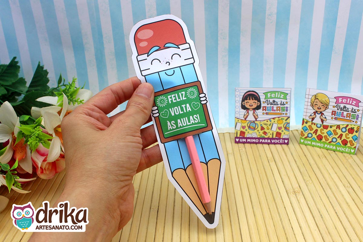 Mão segurando cartão porta-lápis gigante azul com rosto de menino e lápis rosa inserido