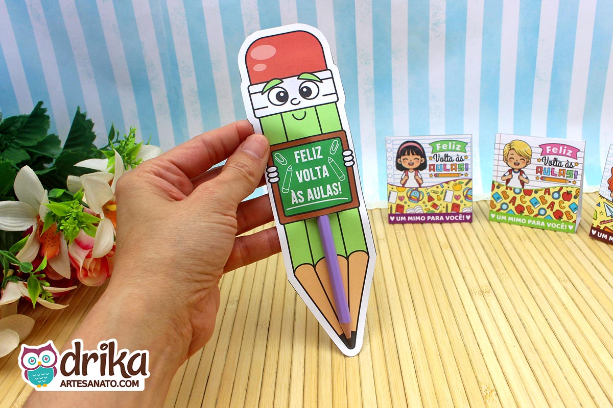 Mão segurando cartão porta-lápis gigante verde com rosto de menino e lápis roxo inserido