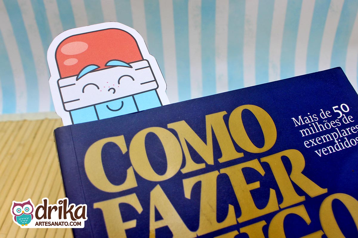 Parte superior de cartão porta-lápis branco e azul com rosto sorridente, usado como marca-páginas em livro azul