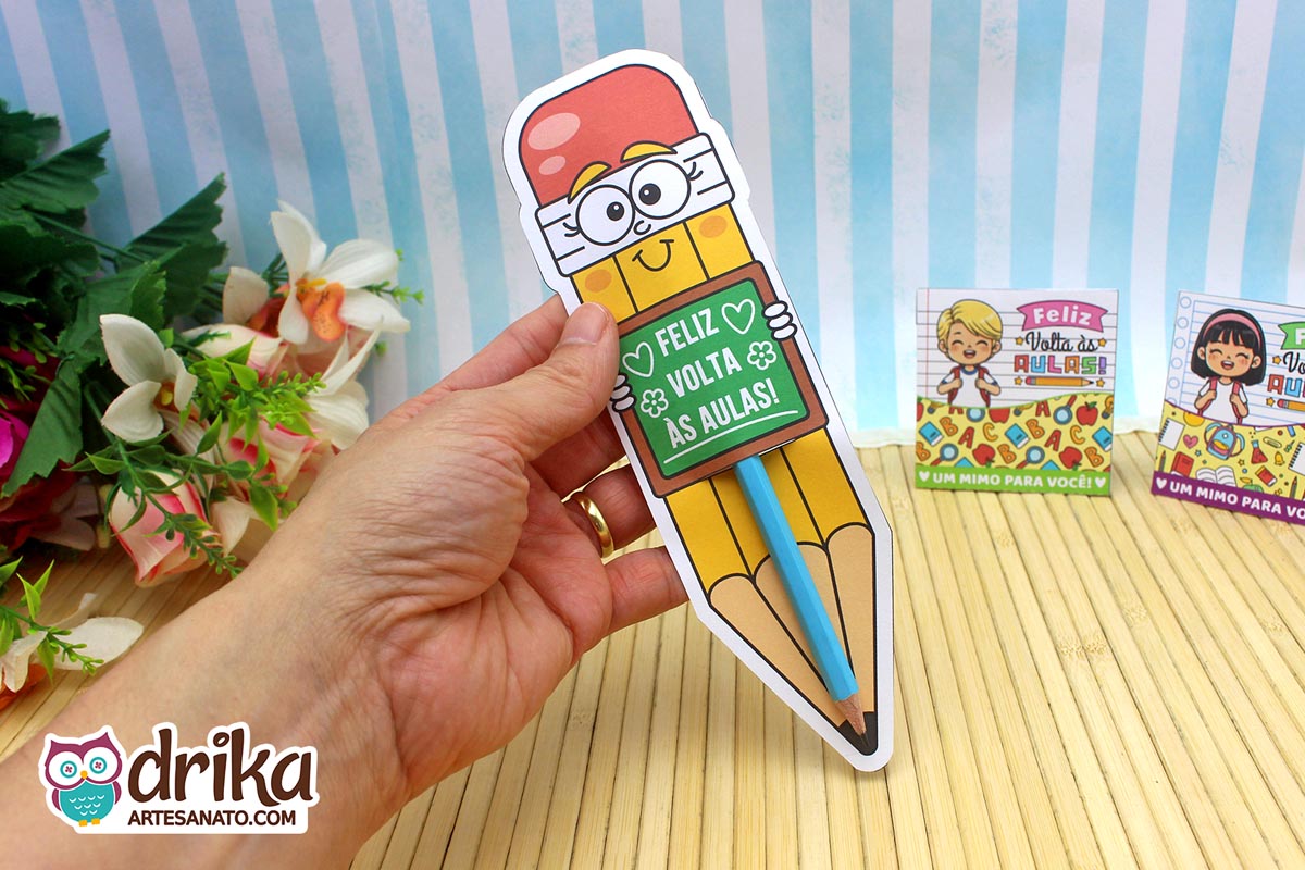 Mão segurando cartão porta-lápis gigante amarelo com rostinho de menina e lápis azul encaixado