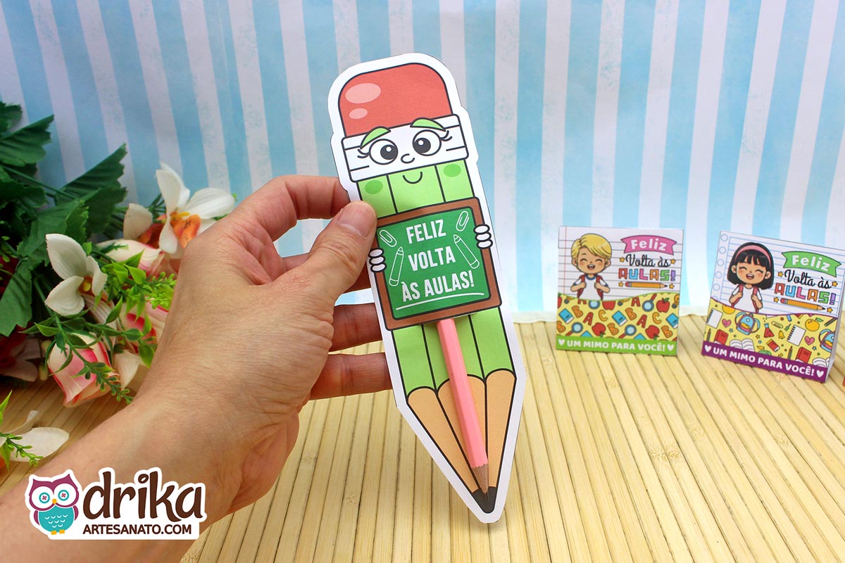 Mão segurando cartão porta-lápis gigante verde com rostinho de menina e lápis rosa encaixado