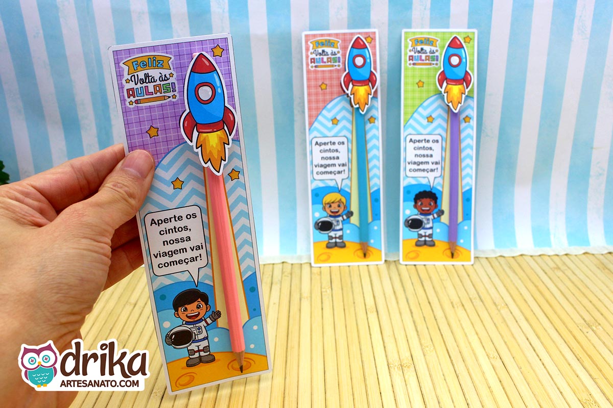 Mão segurando cartão porta-lápis de astronauta menino de cabelo preto liso, com lápis rosa e foguete 3D