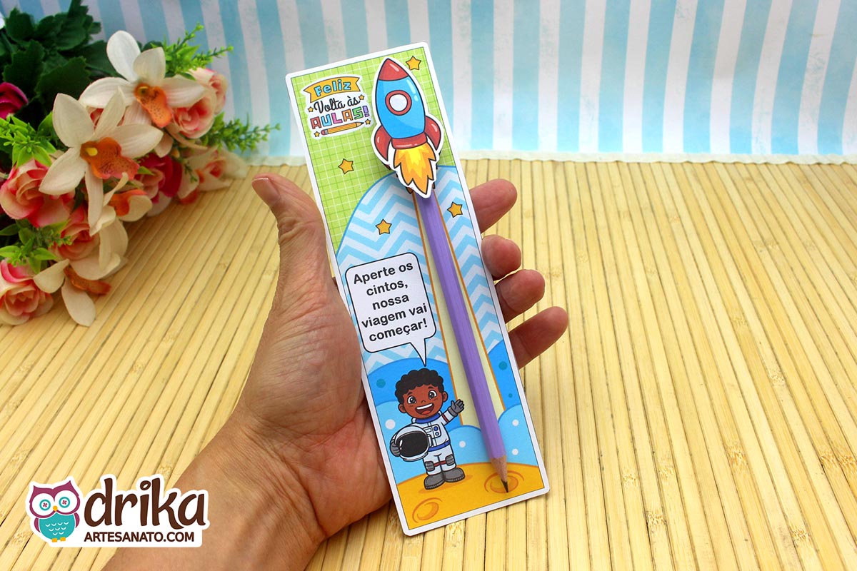 Mão segurando cartão porta-lápis com astronauta menino de cabelo crespo, lápis roxo e foguete 3D