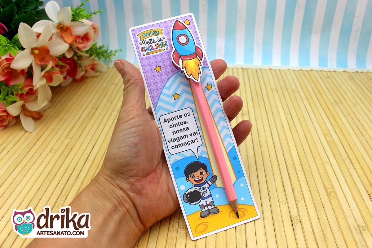 Mão segurando cartão porta-lápis com astronauta menino de cabelo preto liso, lápis rosa e foguete 3D