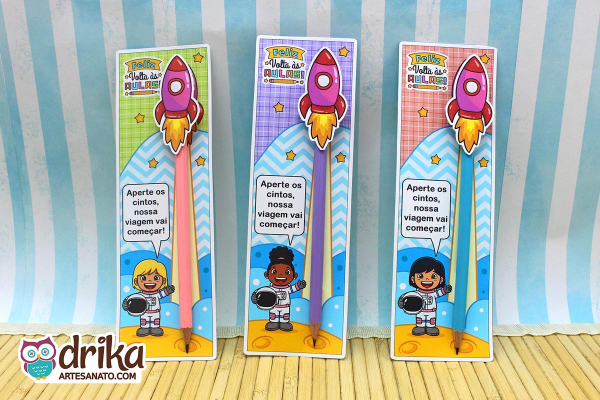 Três cartões porta-lápis com meninas astronautas de cabelos e cores de fundo variados, com lápis