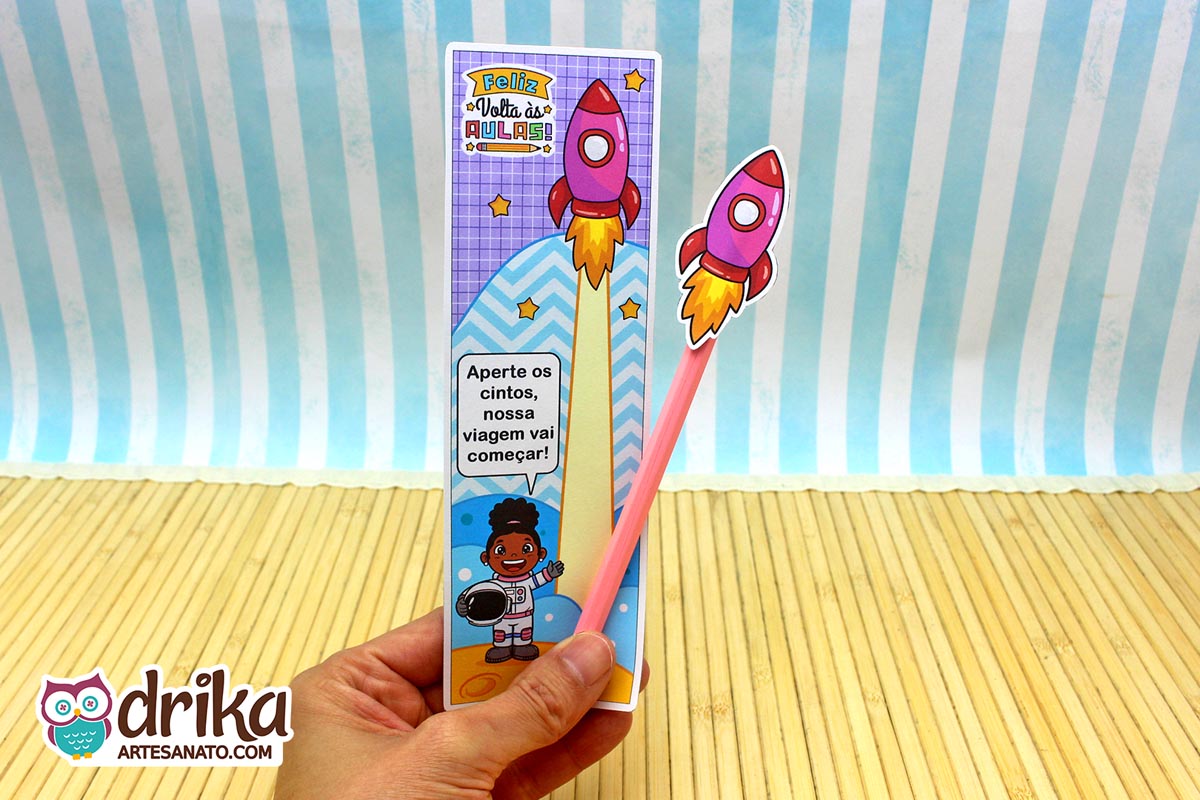Mão segurando cartão porta-lápis de menina astronauta de cabelo crespo com foguete rosa em lápis rosa