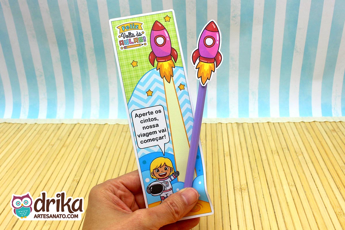 Mão segurando cartão porta-lápis de menina astronauta loira com foguete rosa em lápis roxo
