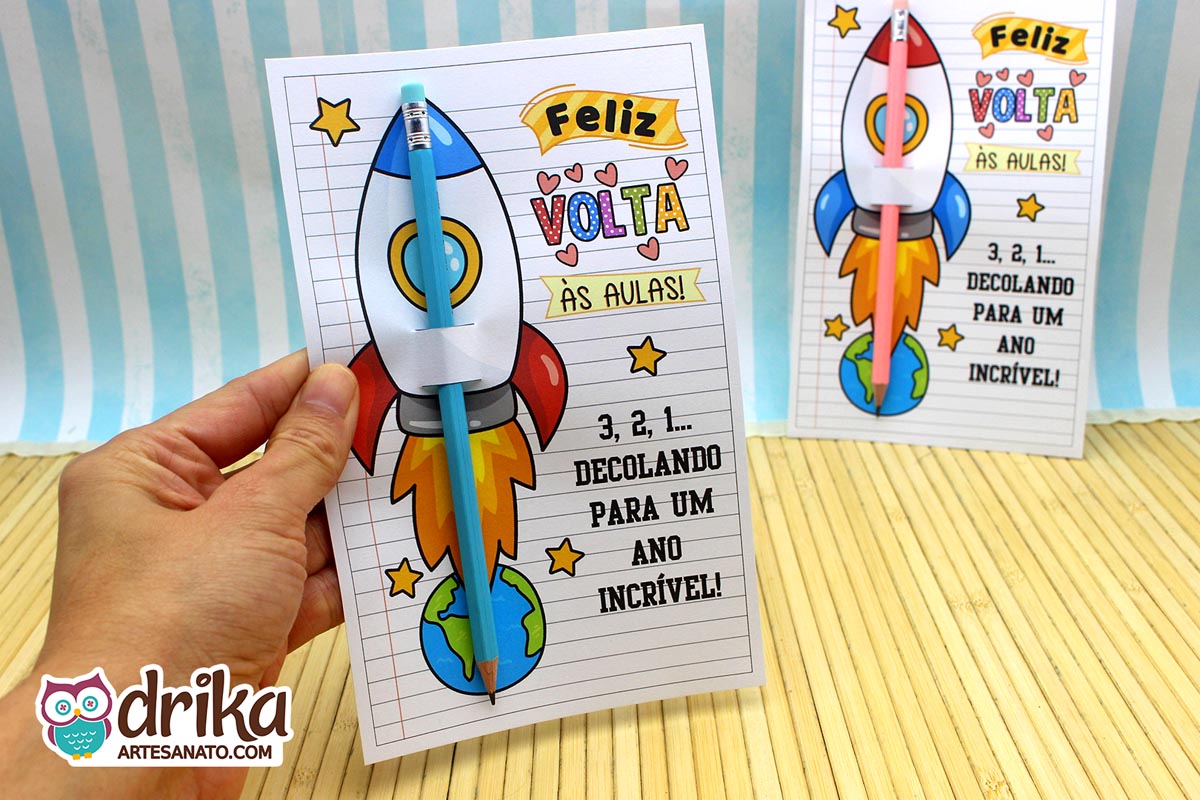 Mão segurando um cartão porta-lápis de foguete azul com lápis azul encaixado, sobre fundo de bambu