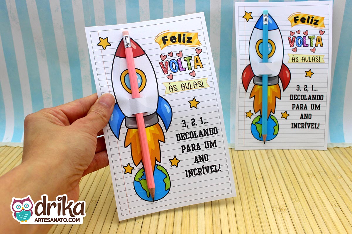 Mão segurando um cartão porta-lápis de foguete vermelho com lápis rosa encaixado, sobre fundo de bambu