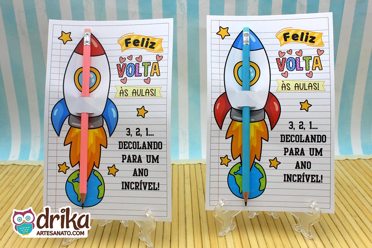 Dois cartões porta-lápis de foguete com lápis rosa e azul encaixados, expostos em suportes transparentes