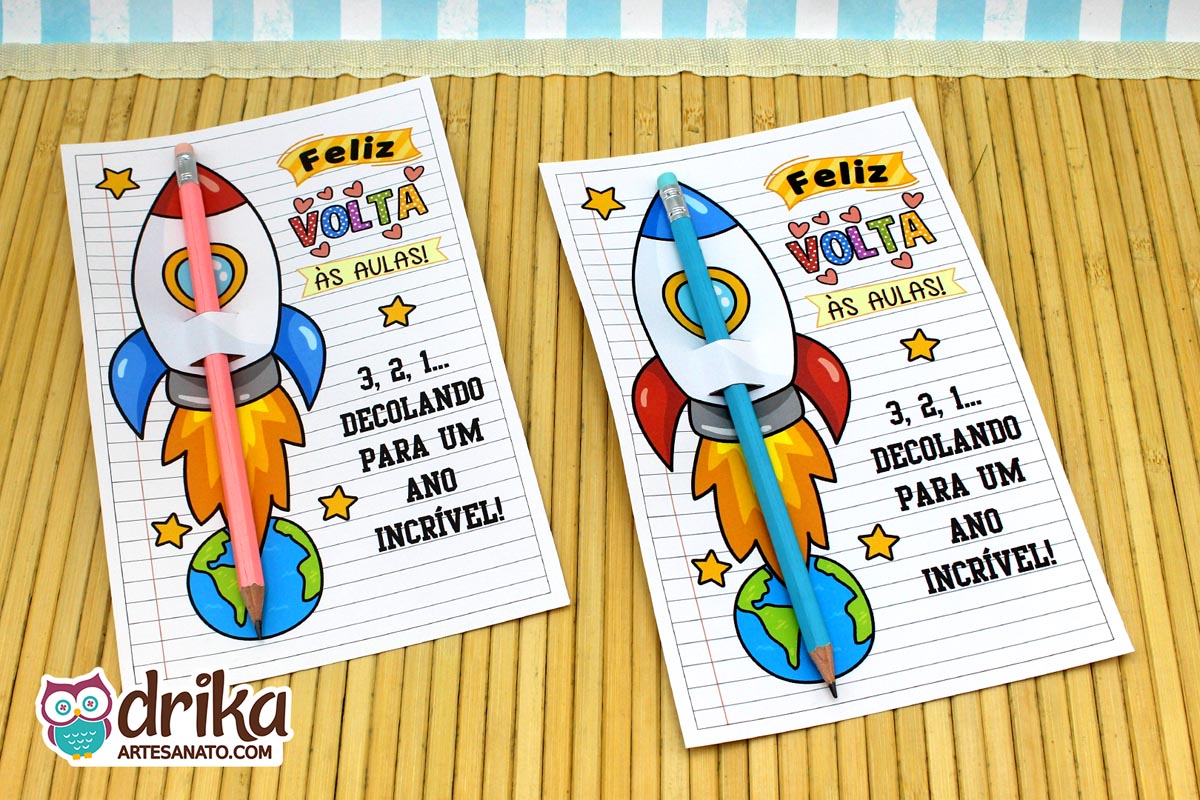 Dois cartões porta-lápis de foguete coloridos, um com lápis rosa e outro com lápis azul, sobre esteira de bambu