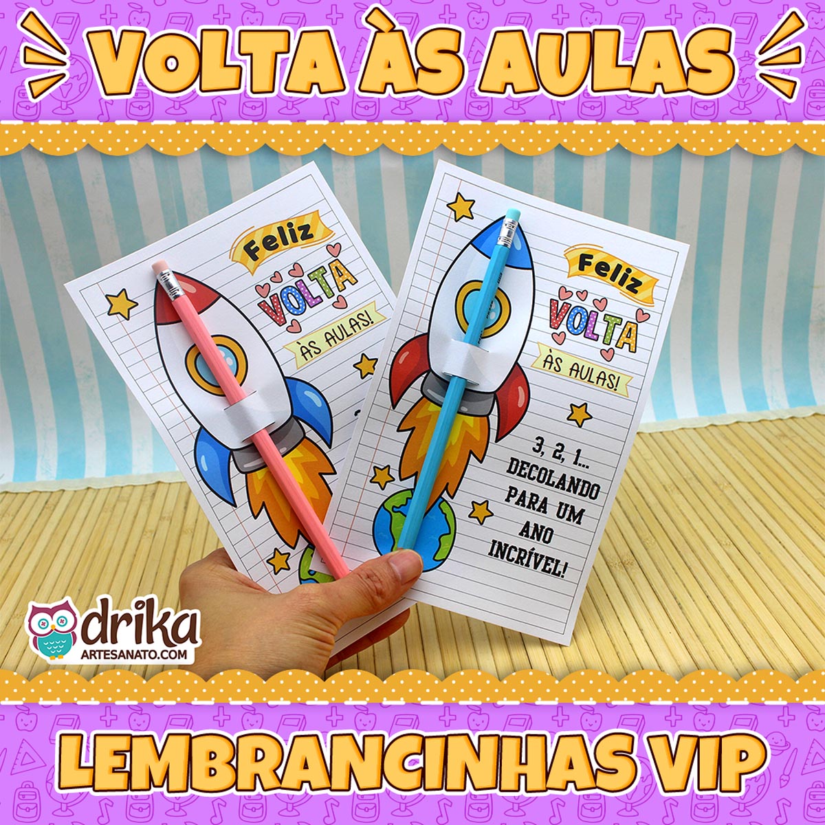 Mão segurando dois cartões porta-lápis de foguete com lápis rosa e azul, com banners "Volta às Aulas" e "Lembrancinhas VIP"