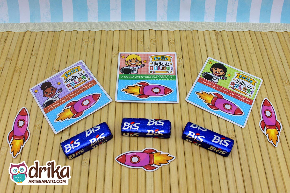 Três cartões porta-bis de astronautas meninas com bis de chocolate e foguetes extras em uma superfície de bambu