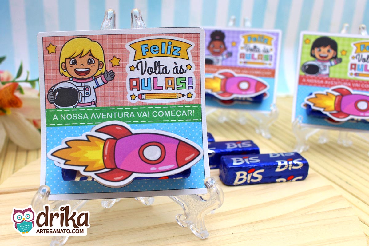 Cartão porta-bis com menina astronauta loira, bis de chocolate e foguete 3D rosa afixado, em cavalete